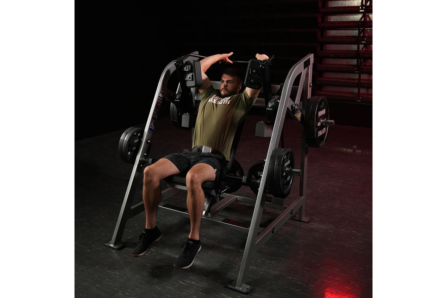 Man using Hammer Strength plate-loaded pullover machine with arms extended, wearing olive shirt and black shorts in gym setti