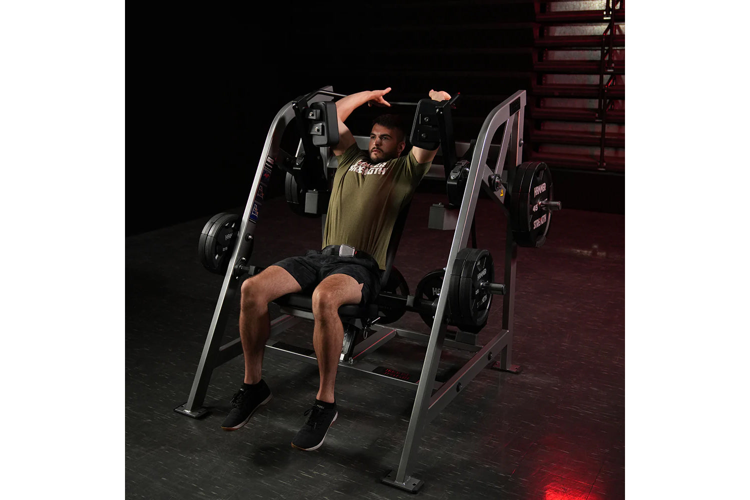 Man using Hammer Strength plate-loaded pullover machine with arms extended, wearing olive shirt and black shorts in gym setti