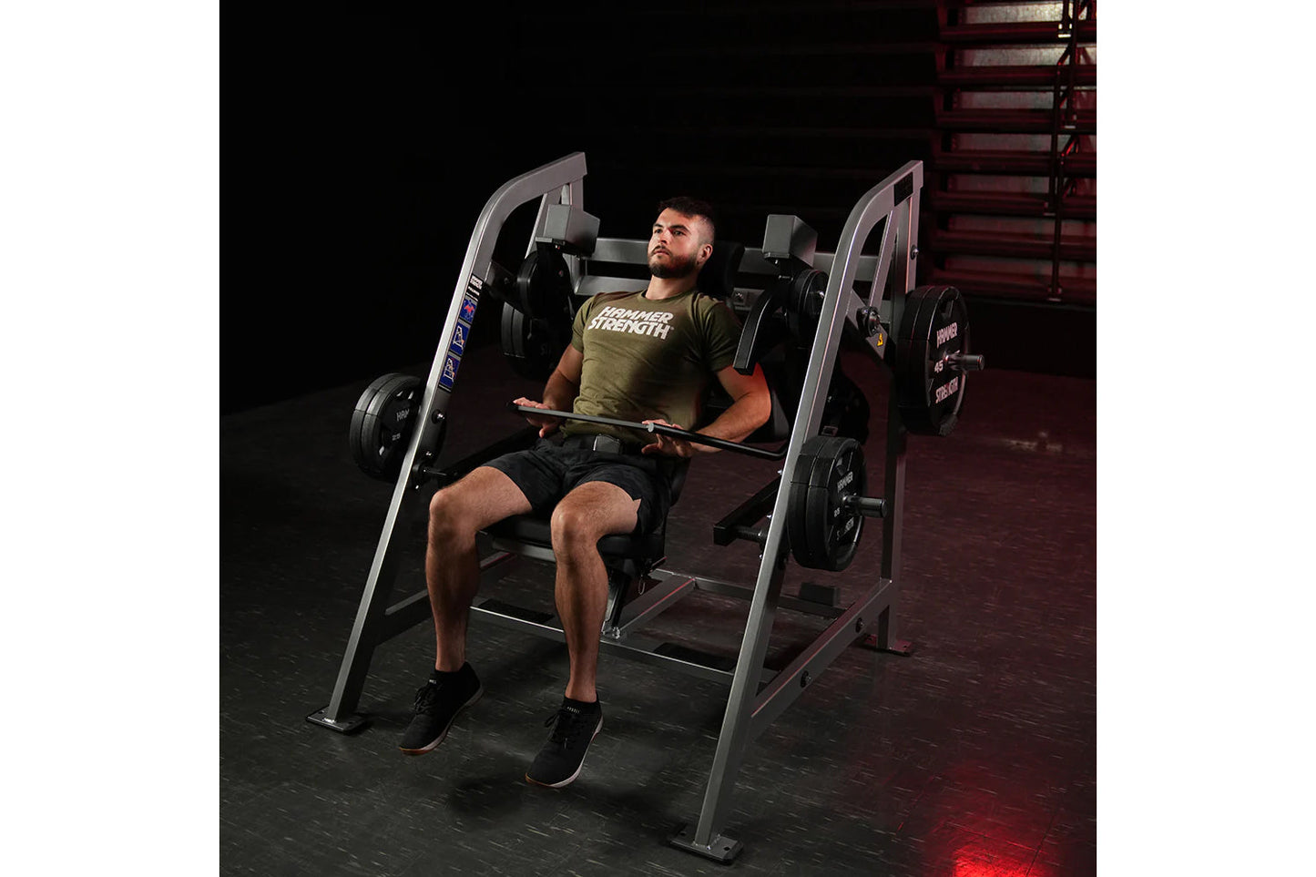 Man using gray Hammer Strength plate-loaded pullover machine in gym, wearing olive green t-shirt and black shorts