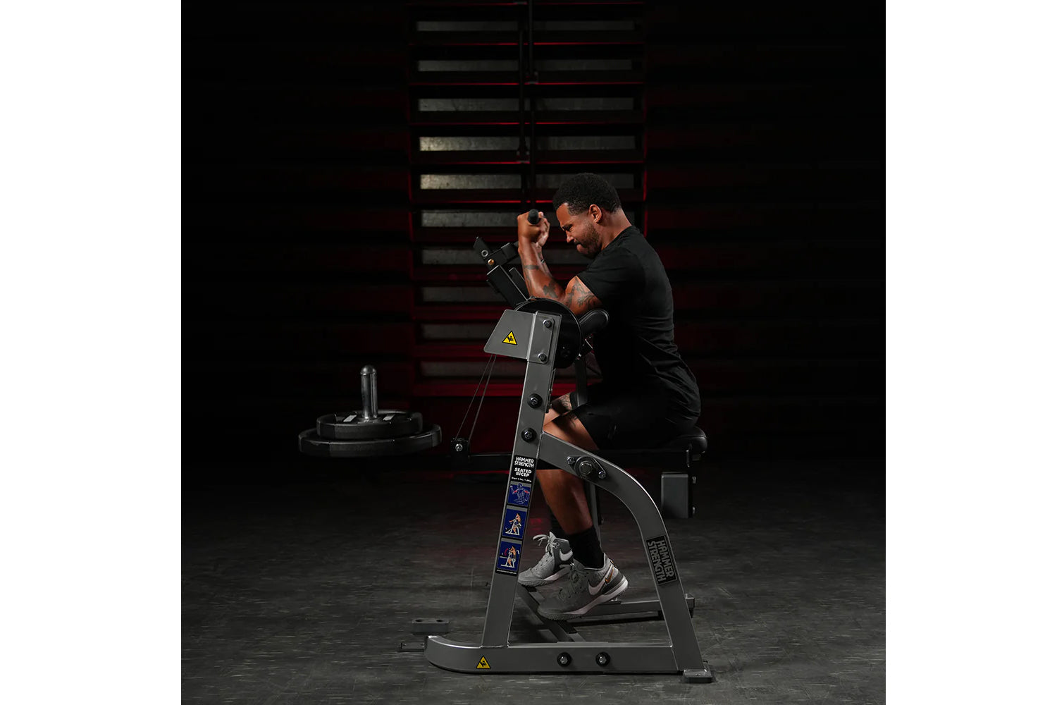 Man using black plate-loaded seated biceps machine in gym setting, demonstrating exercise form with weights loaded on machine