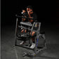 Man using black plate-loaded seated biceps machine with padded arm supports and pull handles against dark background