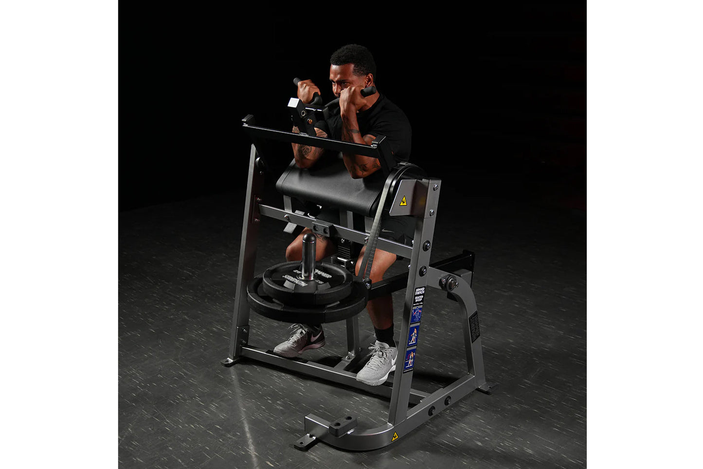 Man using black plate-loaded seated biceps machine with padded arm supports and pull handles against dark background