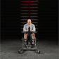 Man seated on Hammer Strength plate-loaded calf raise machine wearing gray long-sleeve shirt and black shorts in gym setting