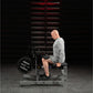 Man in gray long-sleeve shirt and black shorts using Hammer Strength plate-loaded seated calf raise machine in gym setting