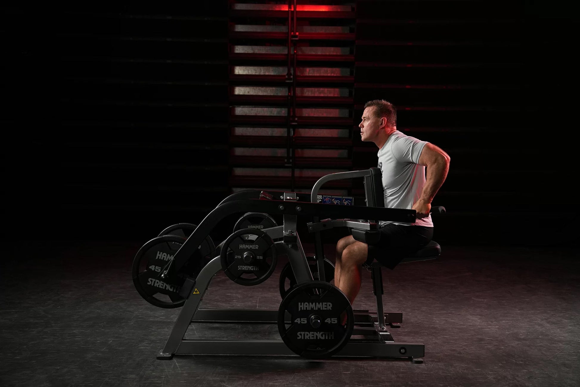 Man wearing gray tank top using Hammer Strength plate-loaded seated dip machine in gym with red lighting