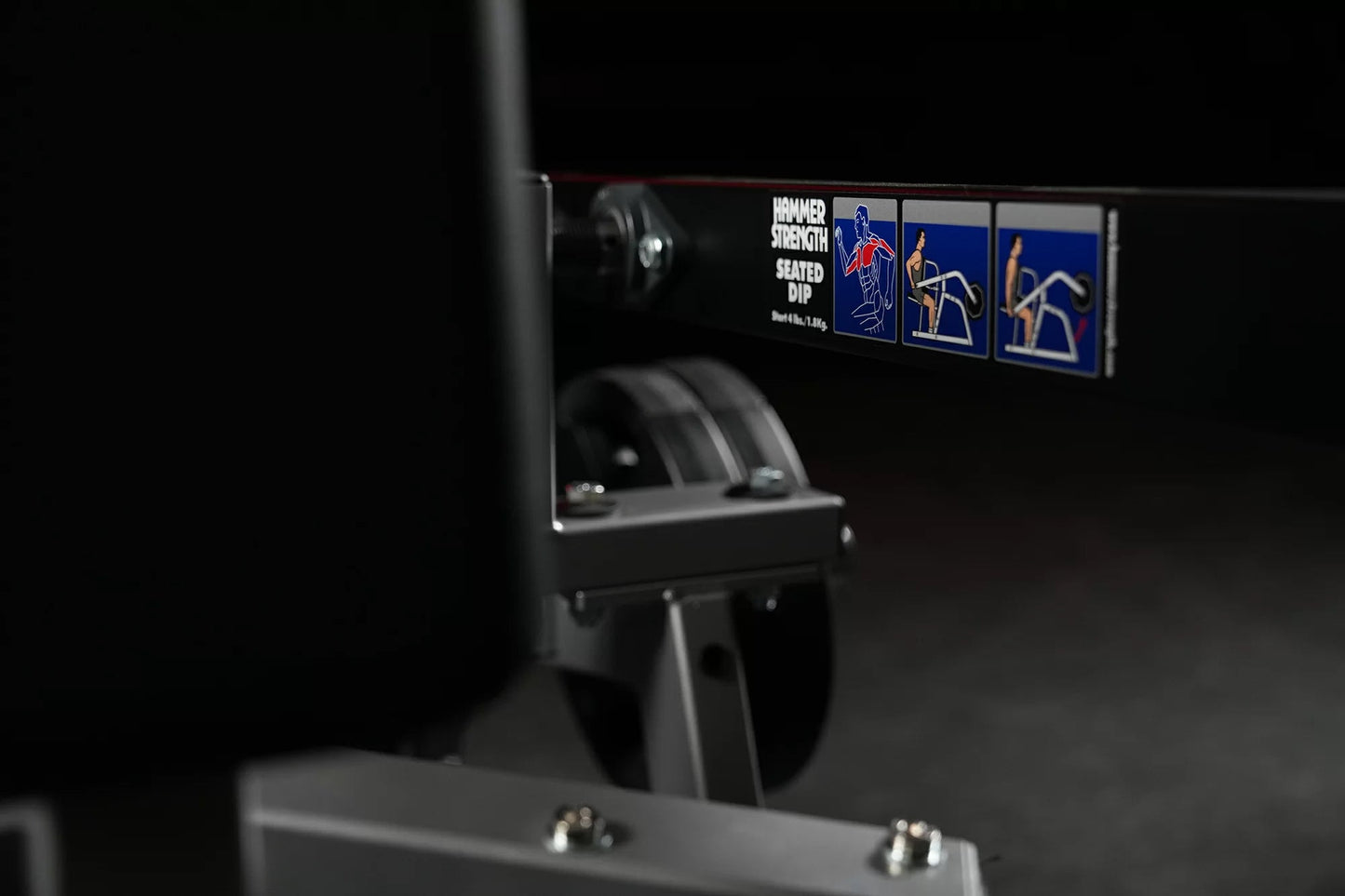 Hammer Strength plate-loaded seated dip machine with instruction label showing exercise form diagrams on black background