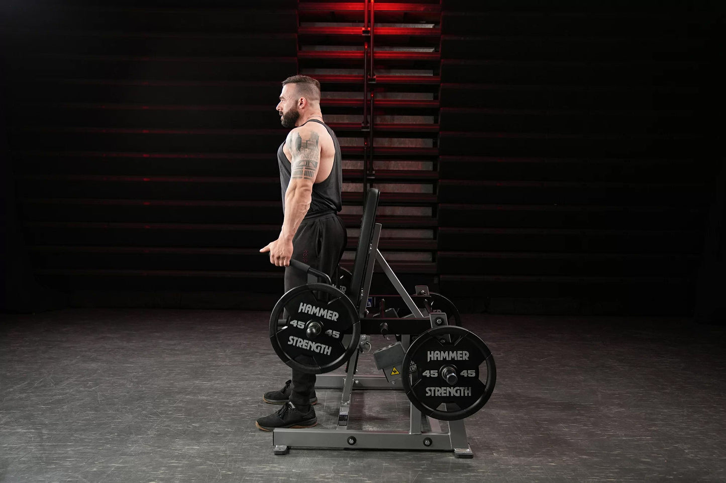 Man using black Hammer Strength plate-loaded shrug machine with 45-pound weight plates in gym setting
