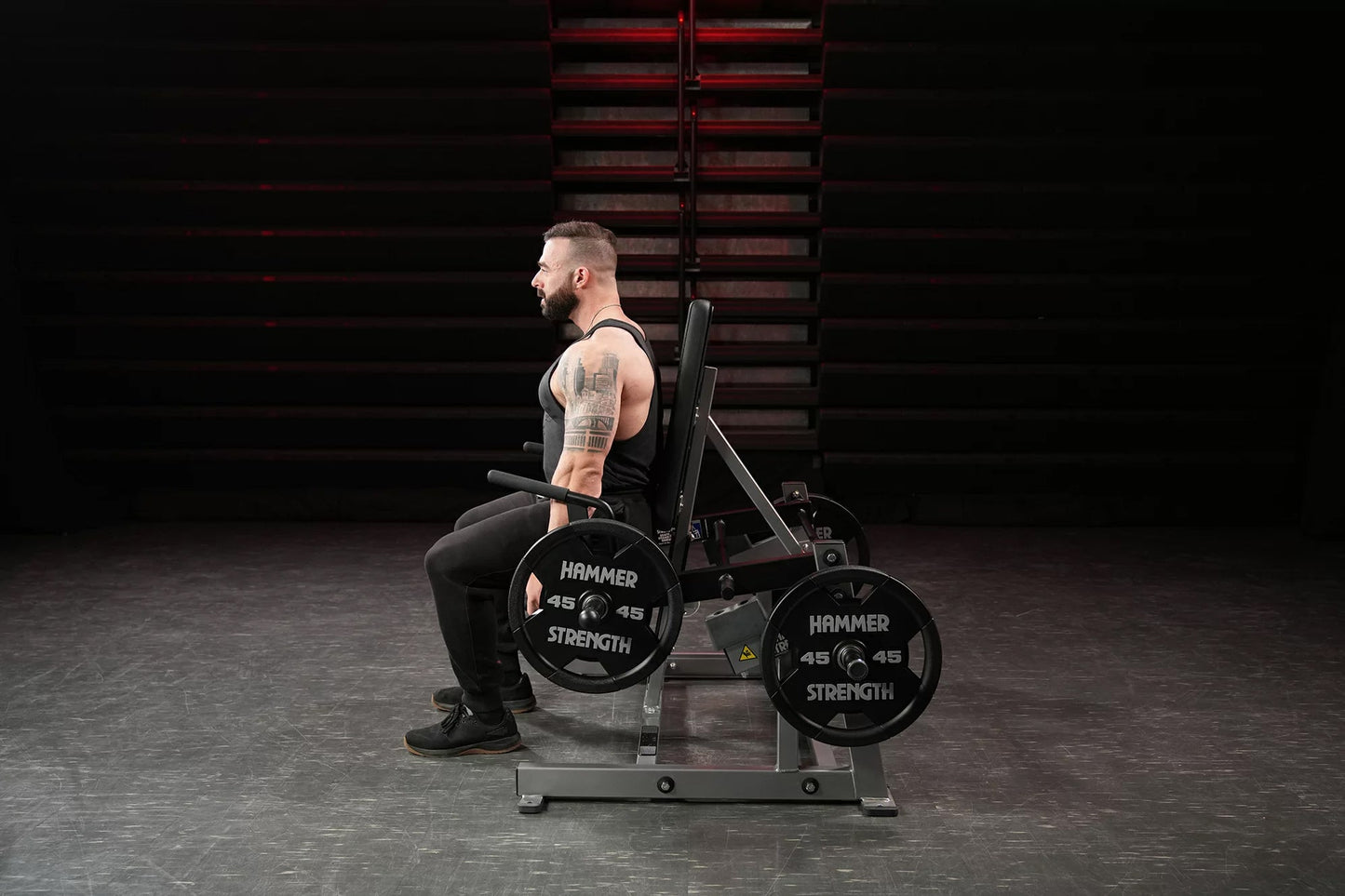 Hammer Strength plate-loaded shrug machine with 45-pound weight plates, shown in gym setting with male model demonstrating us