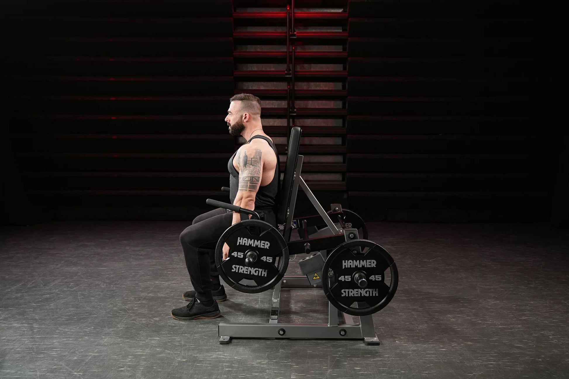 Hammer Strength plate-loaded shrug machine with 45-pound weight plates, shown in gym setting with male model demonstrating us