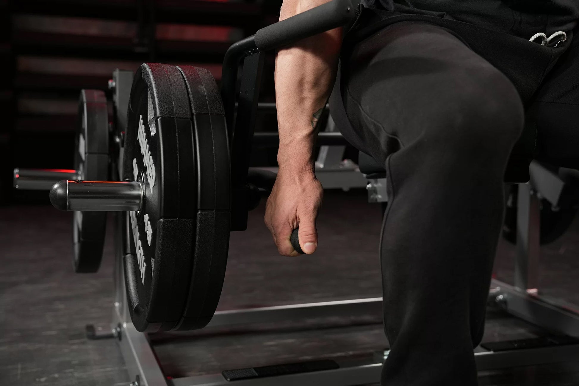 Person in black athletic wear using plate-loaded shrug machine with weighted plates in gym setting