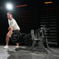 Man performing high pull exercise on black plate-loaded Hammer Strength machine in gym setting with neon lighting