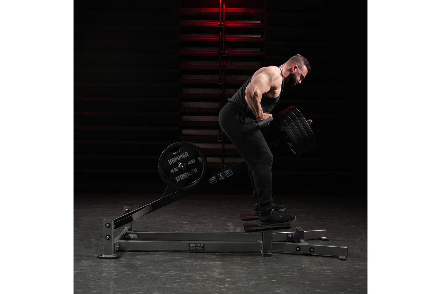 Muscular man performing bent-over row exercise on black Hammer Strength plate-loaded T-bar machine in gym setting
