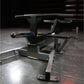 Black plate-loaded T-bar row machine with padded handlebar, cylindrical weight sleeve, and footplate in gym setting