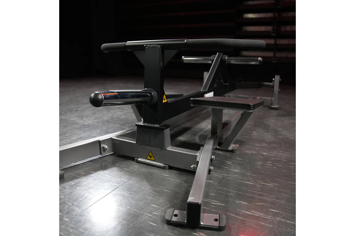 Black plate-loaded T-bar row machine with padded handlebar, cylindrical weight sleeve, and footplate in gym setting