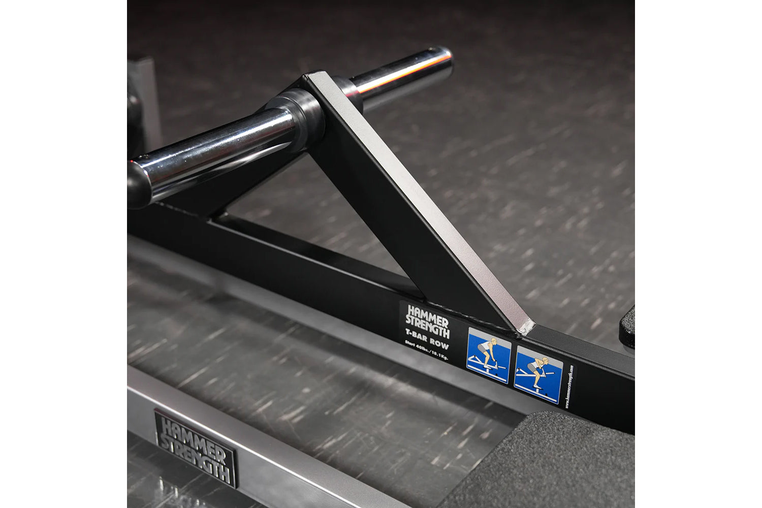 Hammer Strength plate-loaded T-bar row machine with chrome handlebar and white grip pad, black frame on dark background