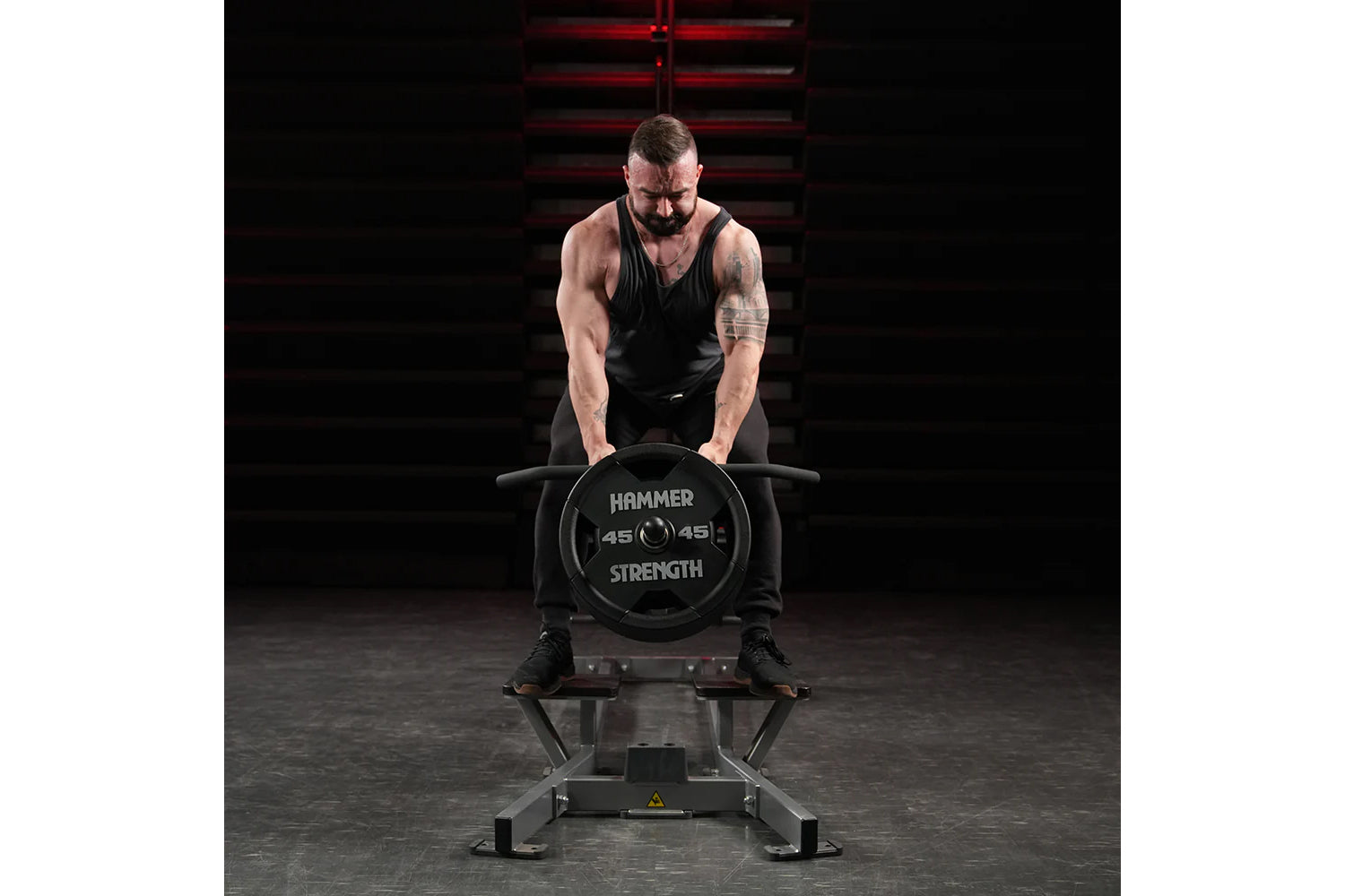 Muscular man in black tank top performing T-bar row exercise on Hammer Strength plate-loaded machine with 45-pound weight pla