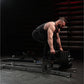 Man performing bent-over rowing exercise on black plate-loaded T-bar machine in gym setting with metal stairs background