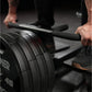 Person using black plate-loaded T-bar row machine with weight plates loaded, gripping handles in gym setting