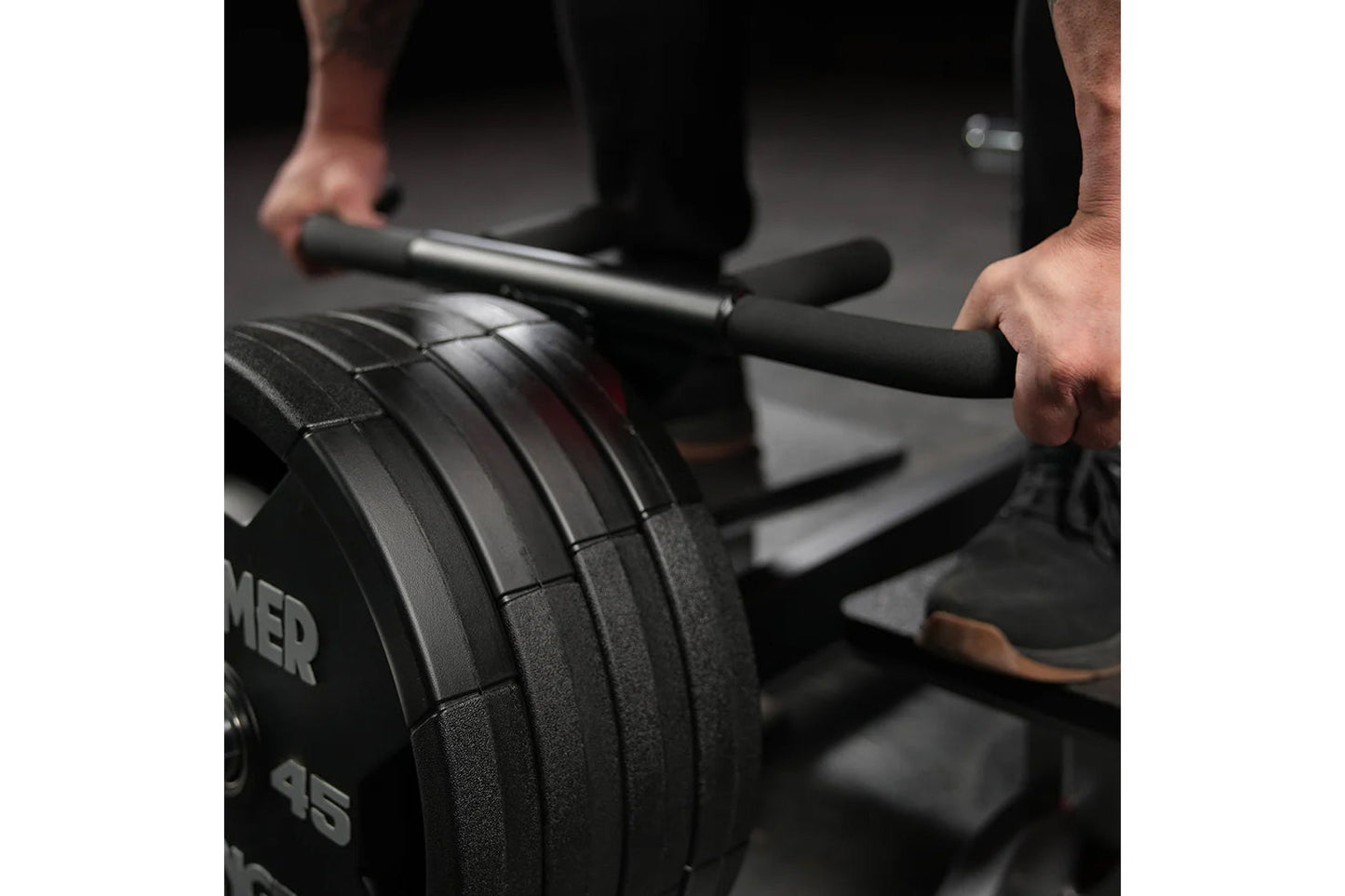 Person using black plate-loaded T-bar row machine with weight plates loaded, gripping handles in gym setting