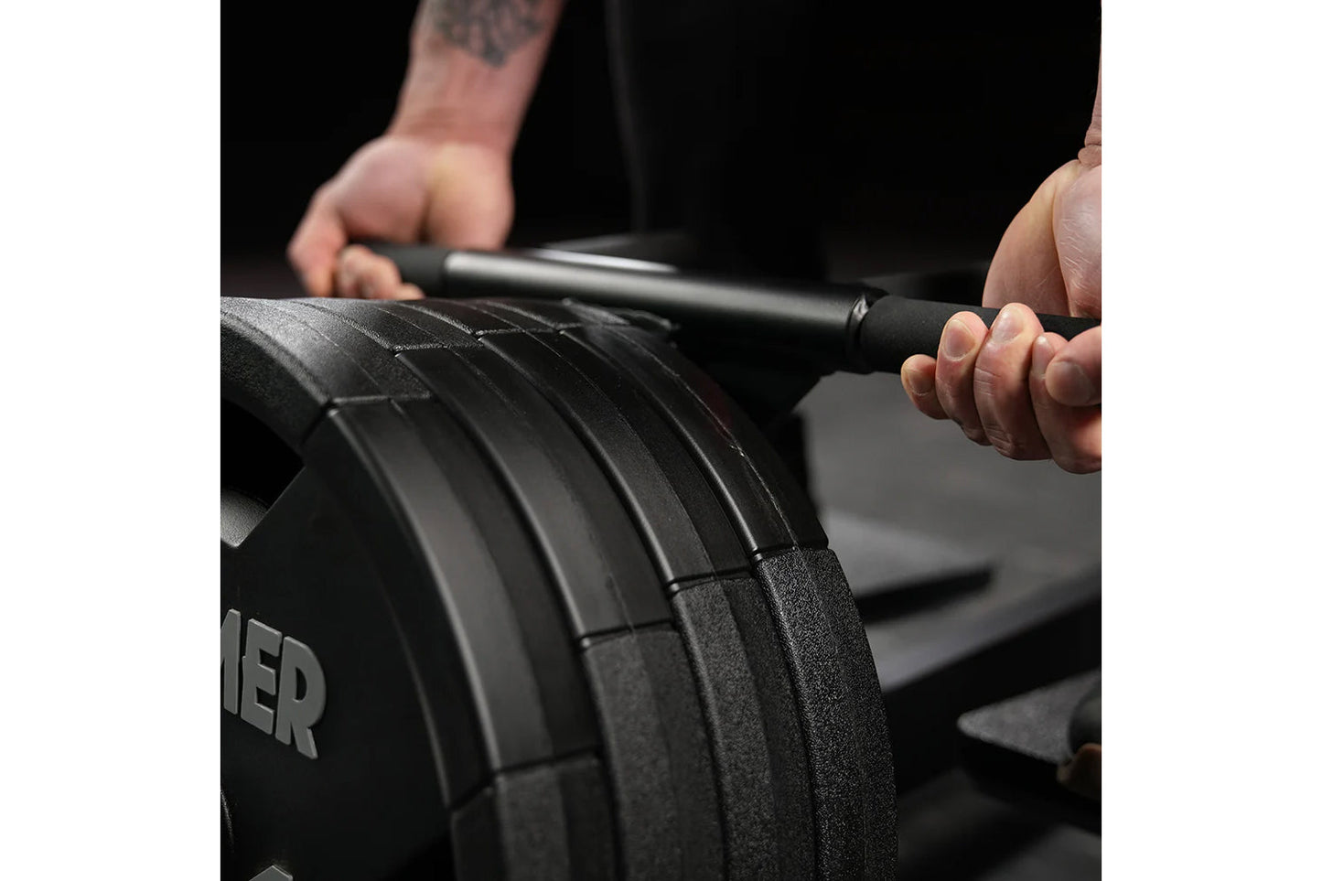 Person holding black plate-loaded T-bar row machine bar with textured grip and weight plates during workout