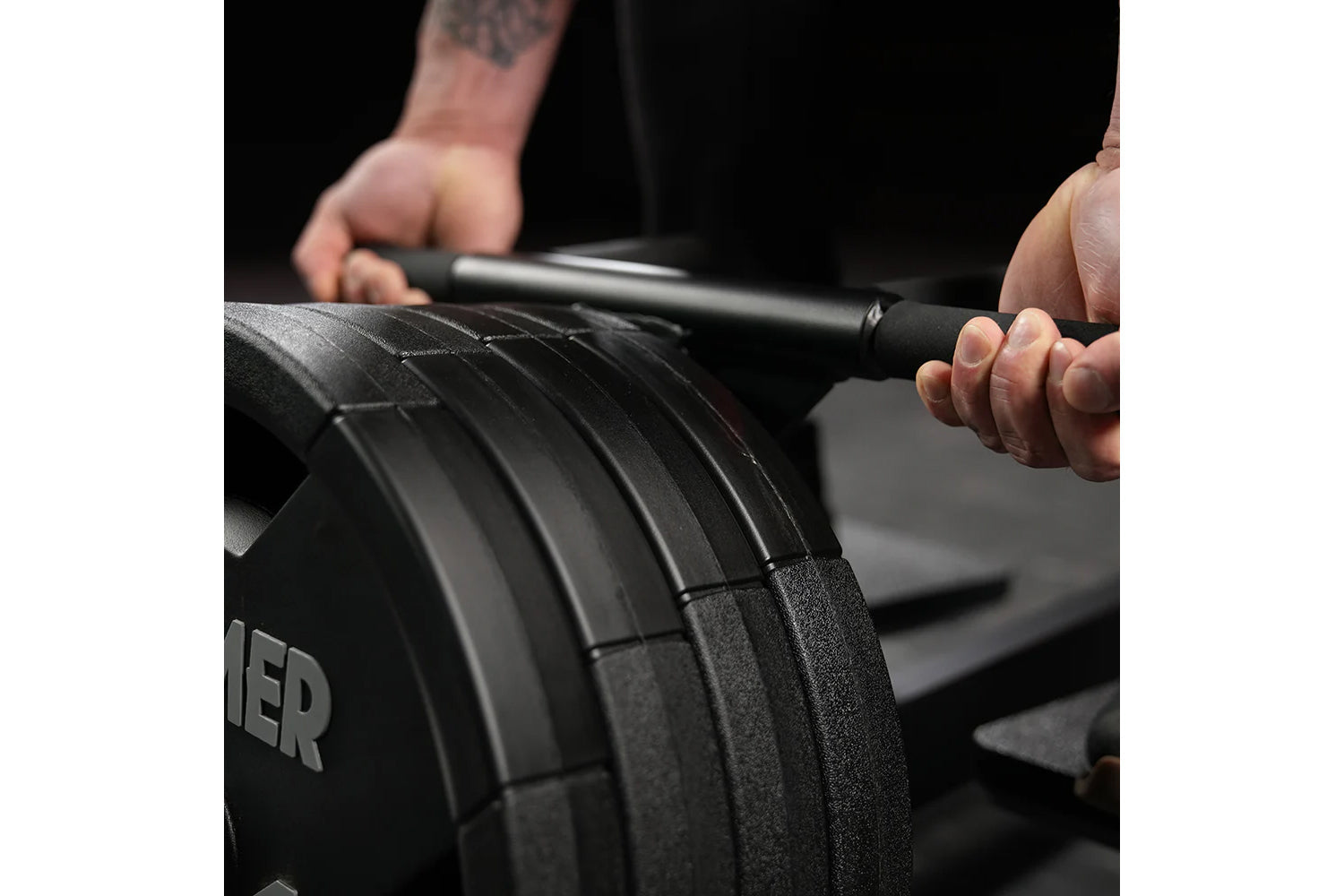 Person holding black plate-loaded T-bar row machine bar with textured grip and weight plates during workout