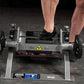 Person in black athletic shoe using Hammer Strength plate-loaded tibia dorsi flexion machine with gray frame and black footpl