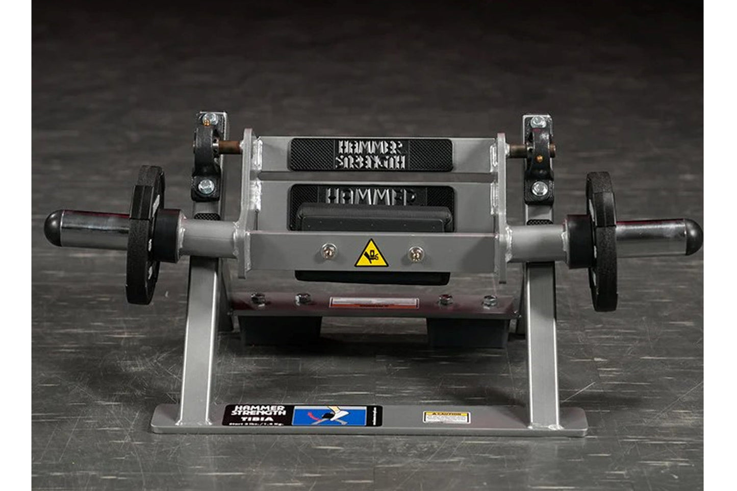 Hammer Strength plate-loaded tibia dorsi flexion machine with gray frame, black foot plates, and yellow caution symbol, front