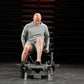 Male model on leg flexion machine wearing gray long-sleeve shirt and shorts, demonstrating exercise position in gym setting