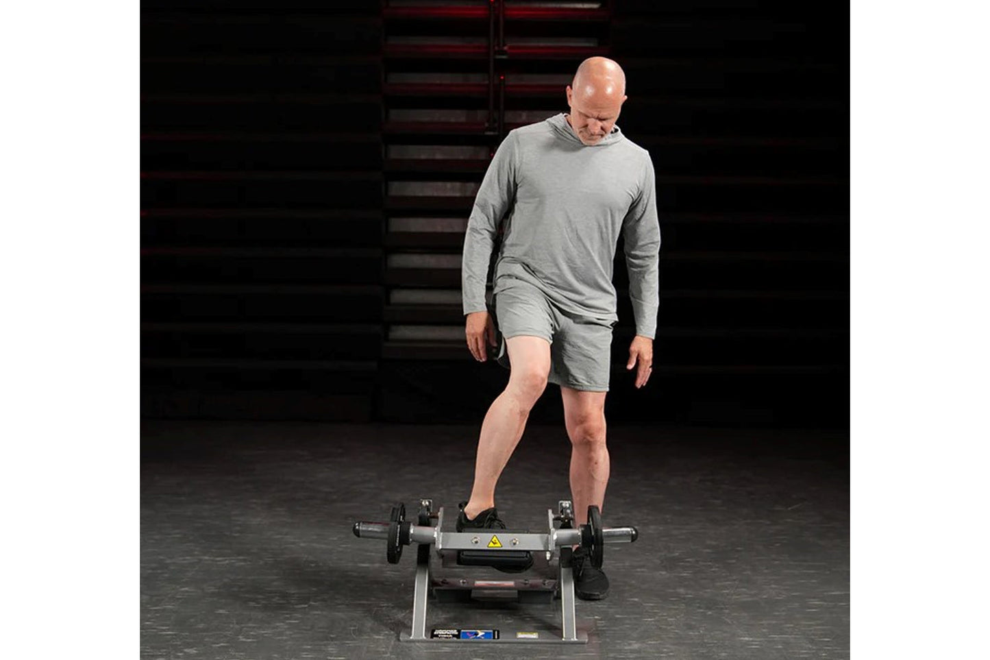 Man wearing gray long-sleeve shirt and shorts using Hammer Strength plate-loaded tibia dorsi flexion bench machine in gym set