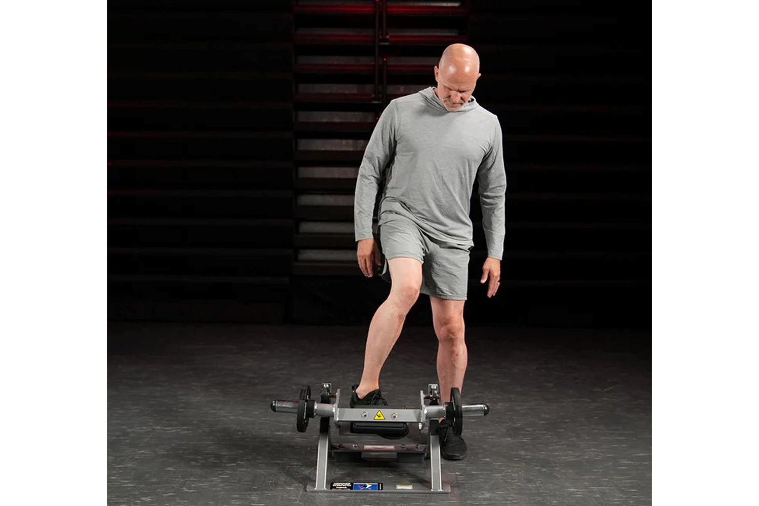 Man wearing gray long-sleeve shirt and shorts using Hammer Strength plate-loaded tibia dorsi flexion bench machine in gym set