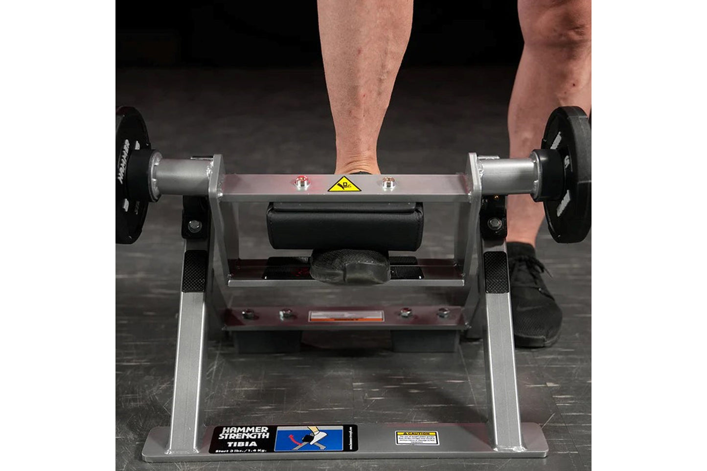 Person performing leg exercise on Hammer Strength plate-loaded tibia dorsi flexion machine with black weight plates attached 