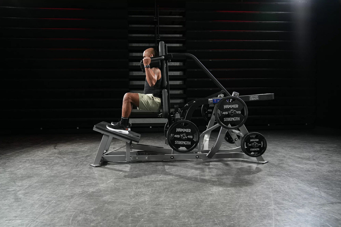 Male athlete performing leg press on black Hammer Strength plate-loaded V-squat machine with weight plates, in gym setting