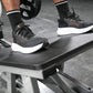 Black and white running shoes with orange accents worn by model on exercise equipment during workout