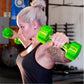 Woman lifting bright green translucent urethane dumbbells in a gym setting, wearing black sports tank top