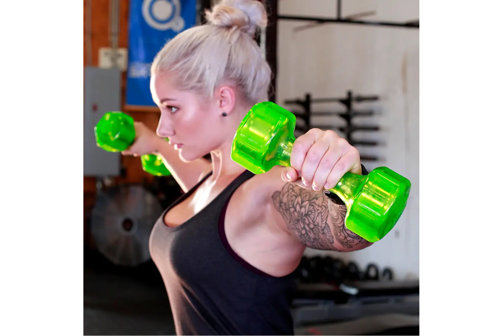 Woman lifting bright green translucent urethane dumbbells in a gym setting, wearing black sports tank top
