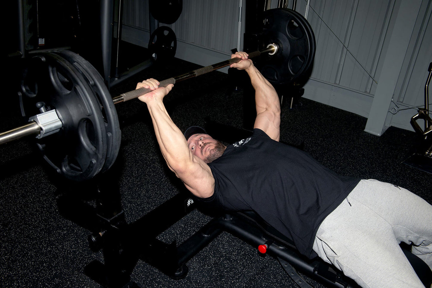 Man performing bench press with black Olympic barbell and weight plates on gym bench