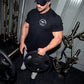 Black short-sleeve t-shirt with white chest graphic worn by man lifting weight plate in gym setting