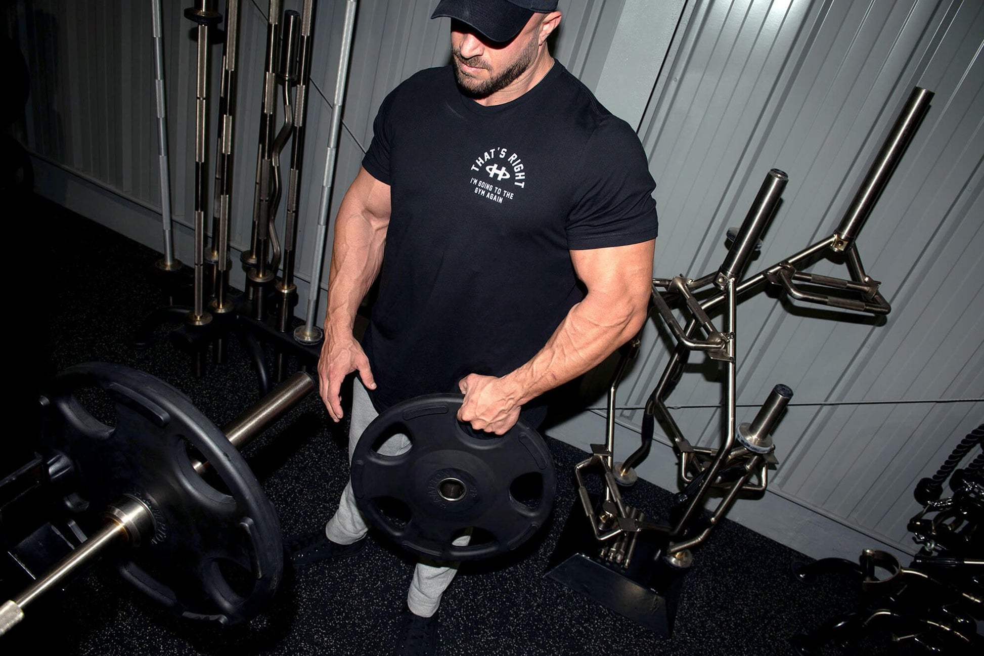 Black short-sleeve t-shirt with white chest graphic worn by man lifting weight plate in gym setting