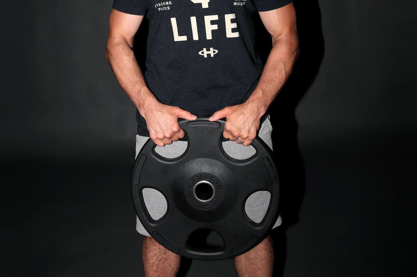 Man wearing black graphic t-shirt holding black Olympic weight plate with gray grip handles, front view