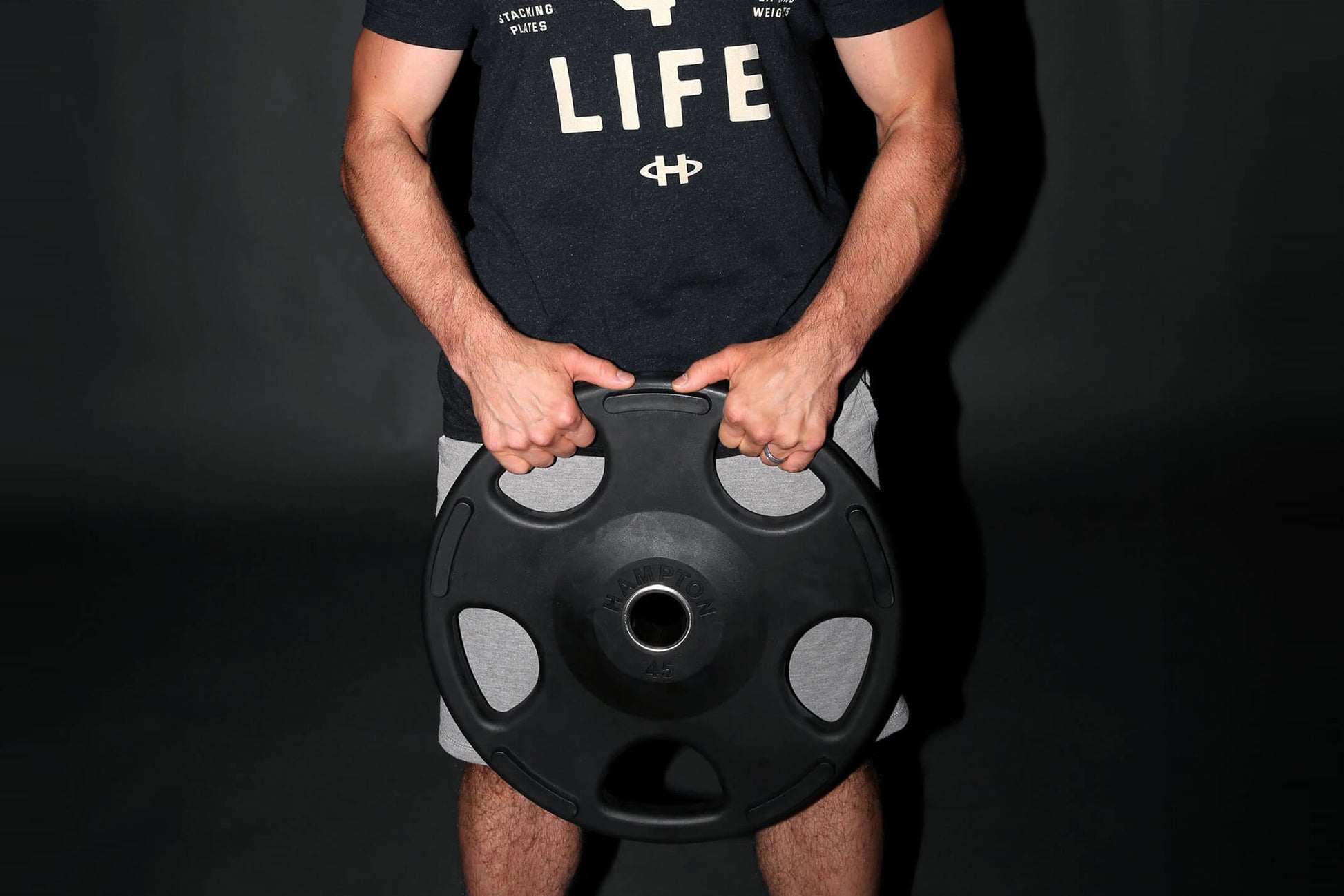 Man wearing black graphic t-shirt holding black Olympic weight plate with gray grip handles, front view