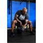 Man wearing black "Bare Speed" graphic t-shirt performing dumbbell exercise in gym with blue wall background