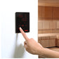 Harvia Spirit digital control panel with red LED display showing temperature and time, mounted on white wall with hand pressi