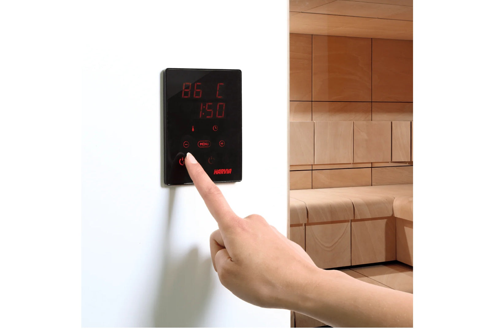 Harvia Spirit digital control panel with red LED display showing temperature and time, mounted on white wall with hand pressi