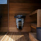 Harvia Spirit electric sauna heater with black metal frame and light stone base mounted on wooden sauna wall interior