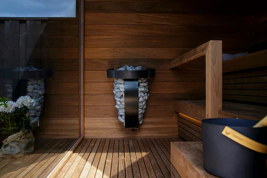 Harvia Spirit electric sauna heater with black metal frame and light stone base mounted on wooden sauna wall interior