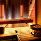 Modern sauna interior with Harvia Spirit heater, wooden benches, neon orange vertical lighting, bucket, ladle, and towel
