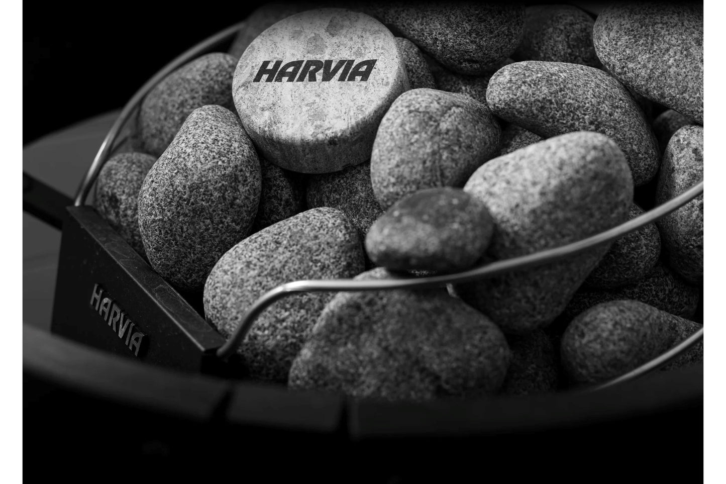 Harvia branded sauna stones in black metal ladle and bucket on dark background