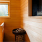 Interior view of wooden sauna with horizontal shiplap walls in warm orange and cream tones, black metal stove with rocks, and