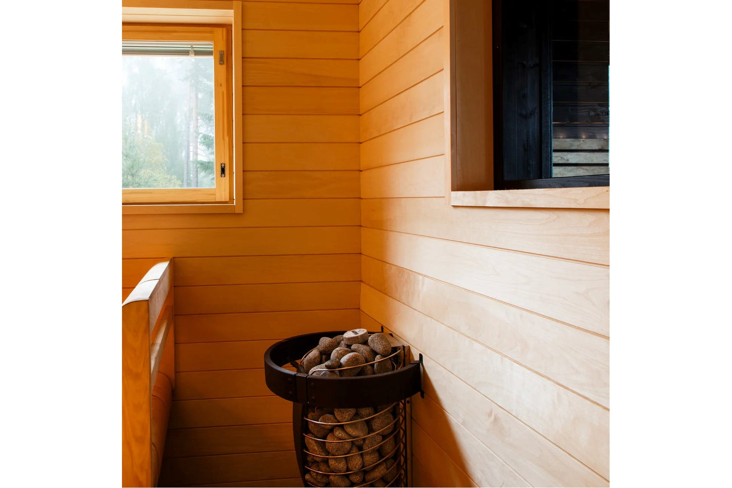 Interior view of wooden sauna with horizontal shiplap walls in warm orange and cream tones, black metal stove with rocks, and