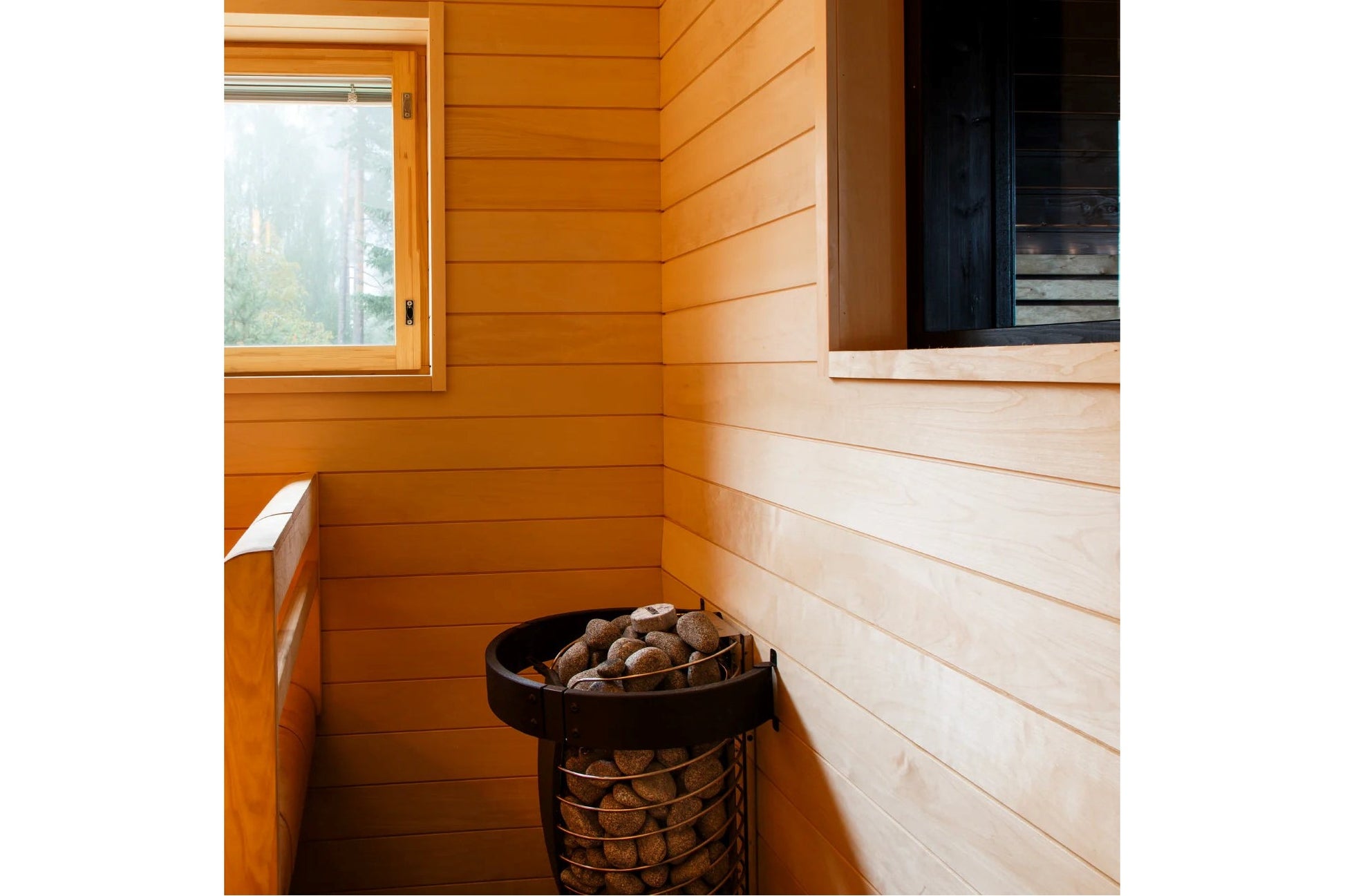 Interior view of wooden sauna with horizontal shiplap walls in warm orange and cream tones, black metal stove with rocks, and
